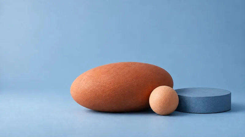Terracotta ellipsoid, slate-blue cylinder and small apricot sphere on a dusty blue backdrop